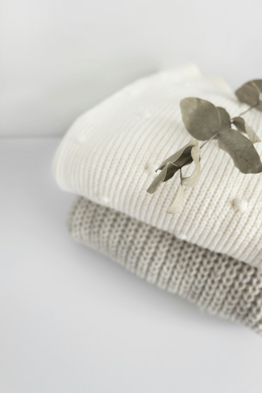 Close-up of folded ivory and grey knits with a eucalyptus sprig