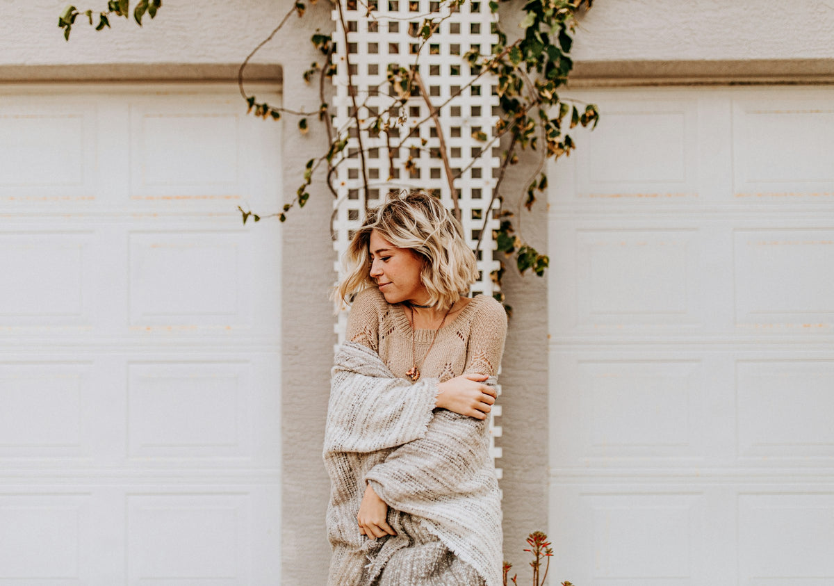 Woman wrapped in a soft oatmeal knit cardigan against white doors