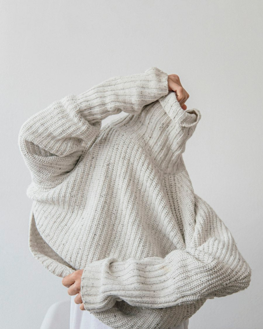 Person pulling on an oversized pale grey knit jumper